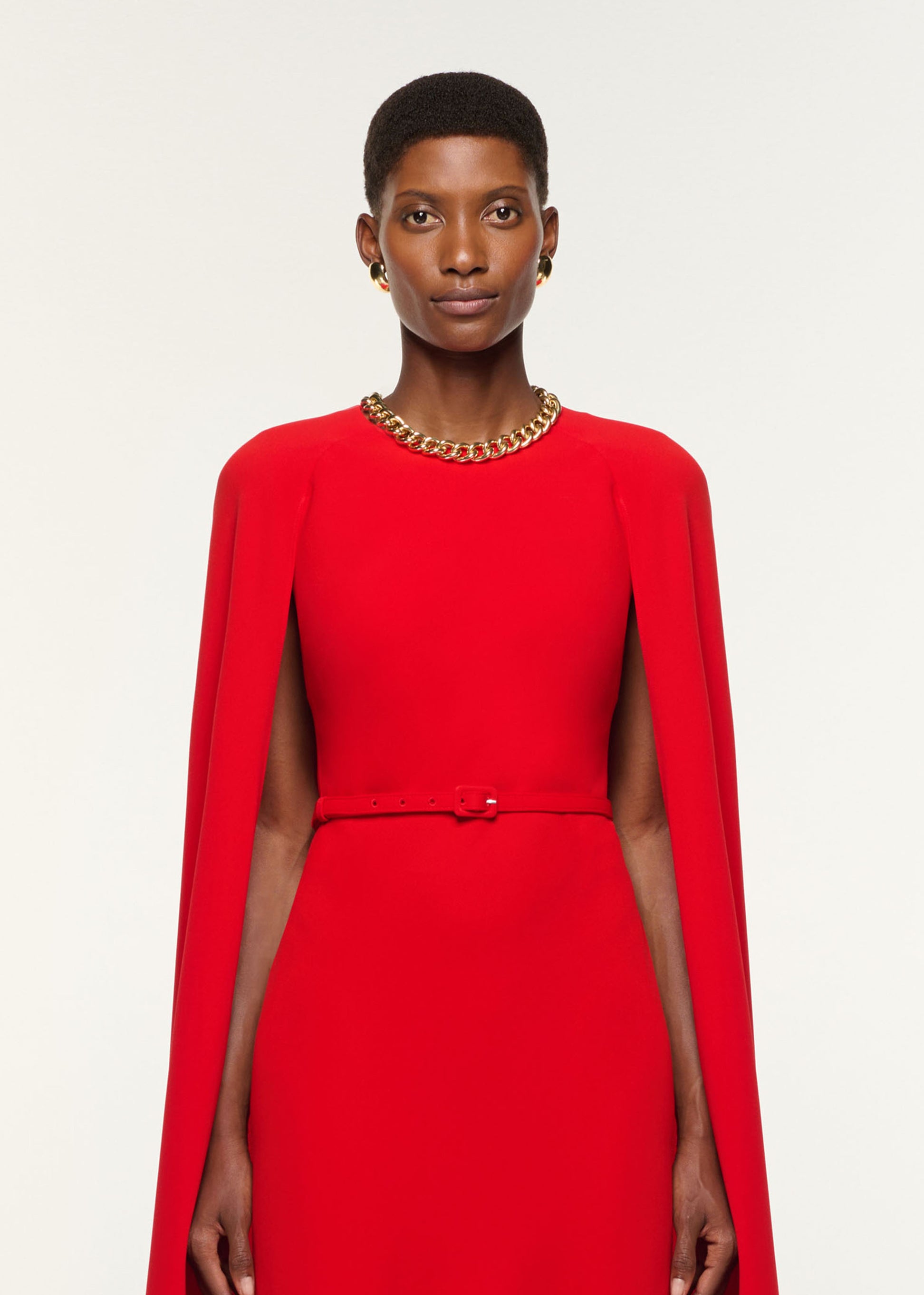 Close up of a model wearing the Light Cady Belted Cape Dress in Red