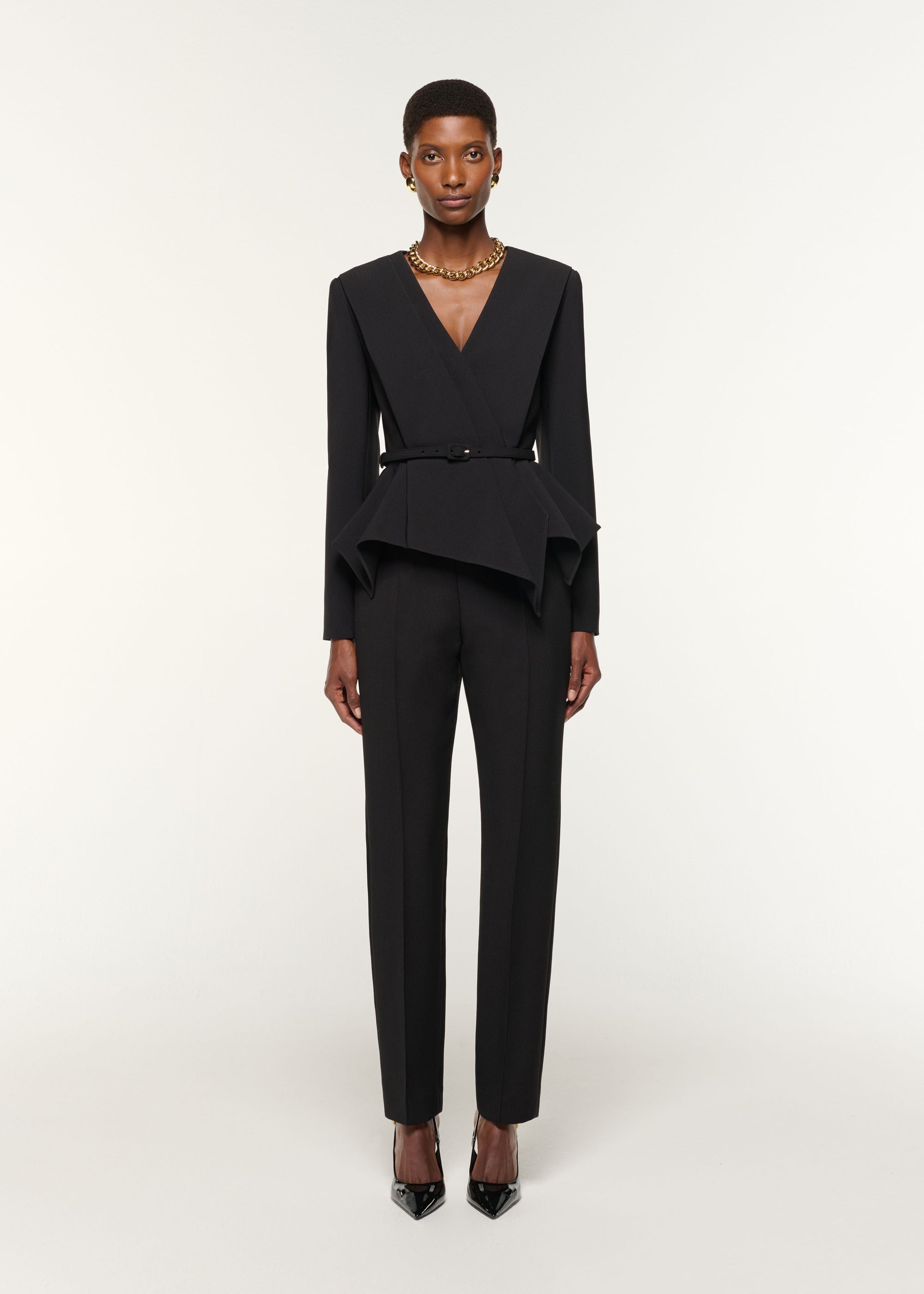 Front view of a model wearing the Asymmetrical Drape Peplum Crepe Jacket in Black