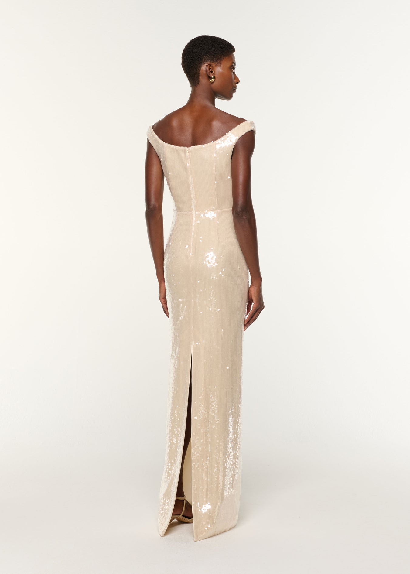 Back view of a model wearing the Off The Shoulder Sequin Gown in Cream