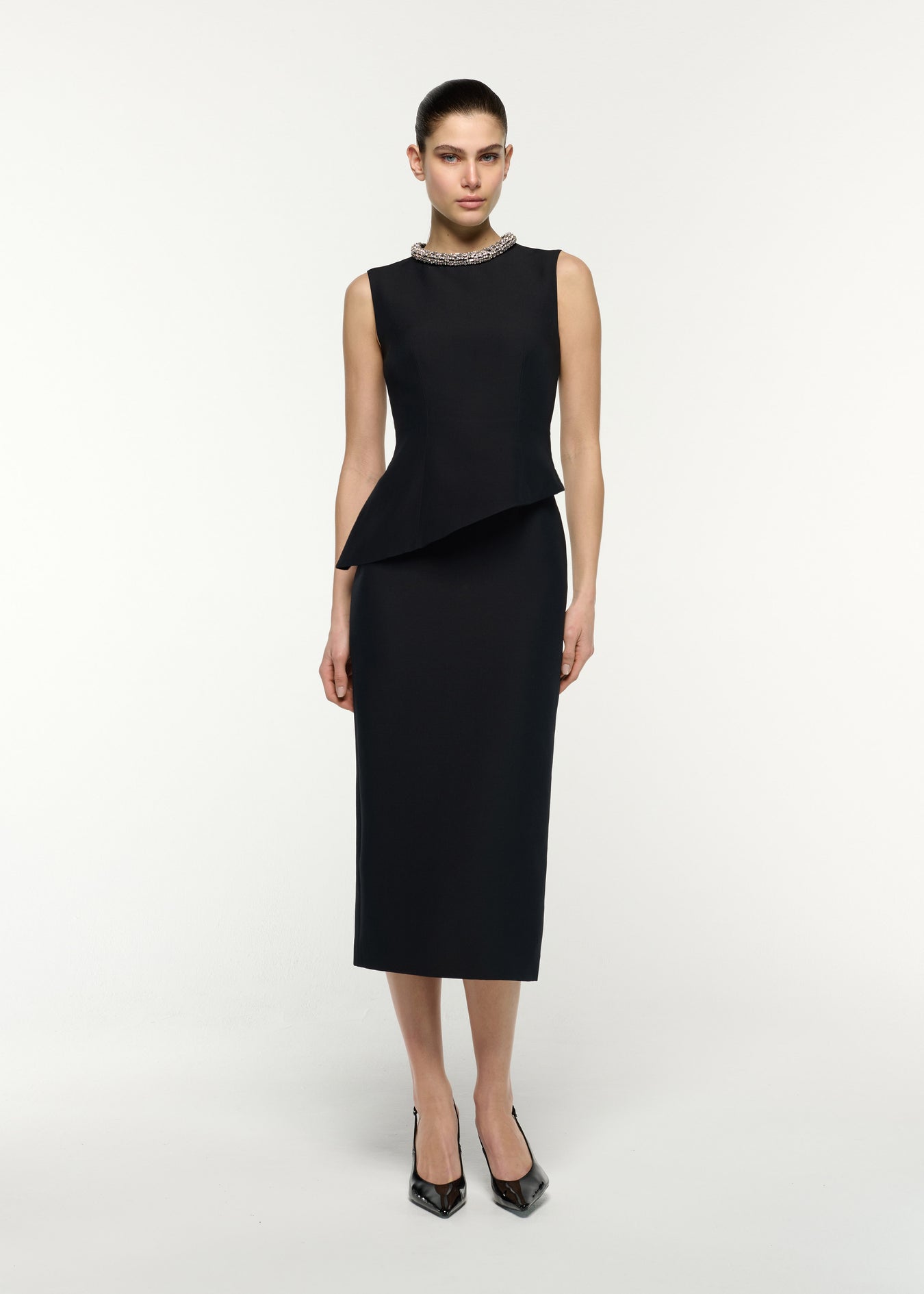 Front view of a model wearing the Crystal Neck Trimmed Asymmetric Peplum Midi Dress in Black 