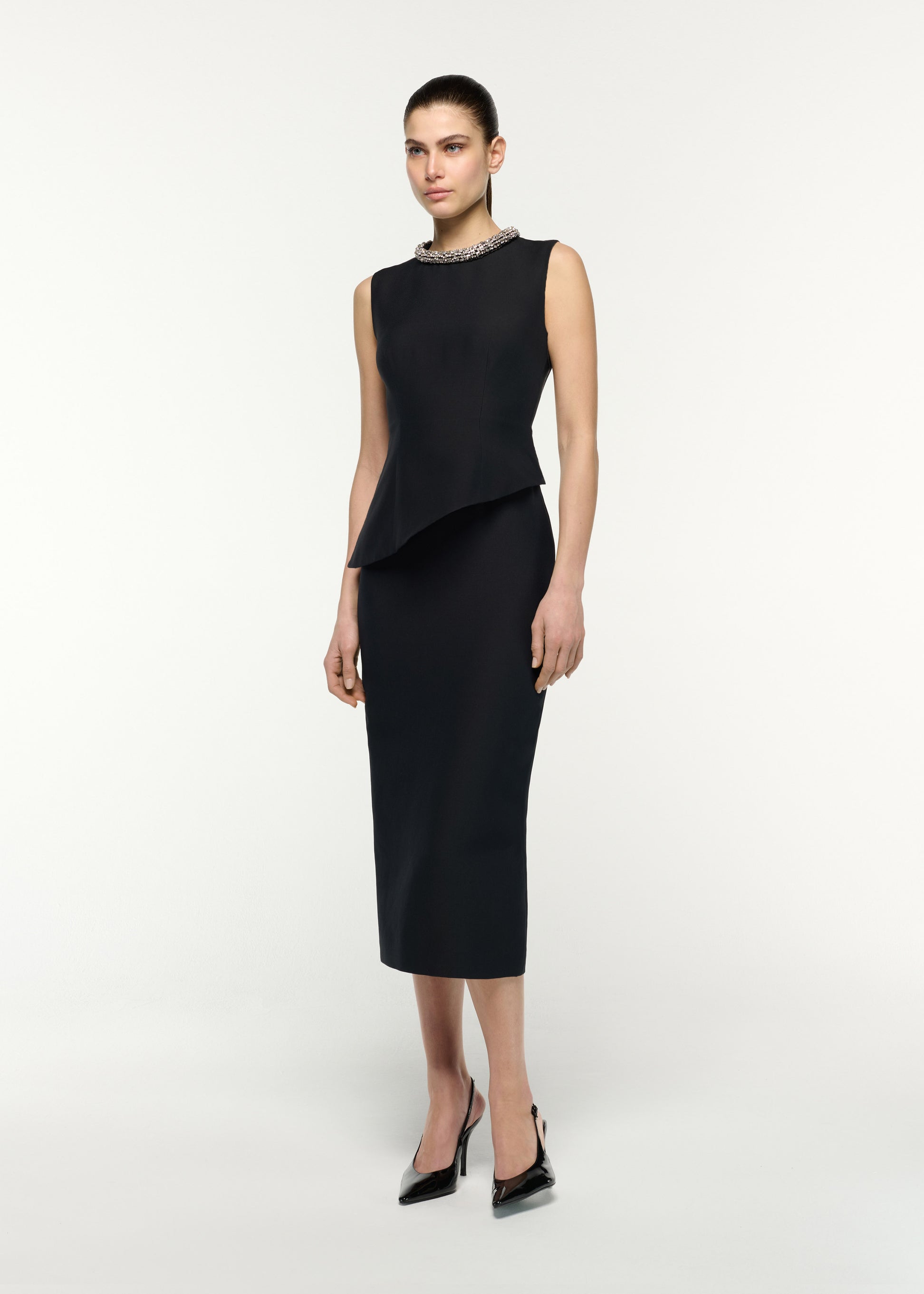 Side view of a model wearing the Crystal Neck Trimmed Asymmetric Peplum Midi Dress in Black 