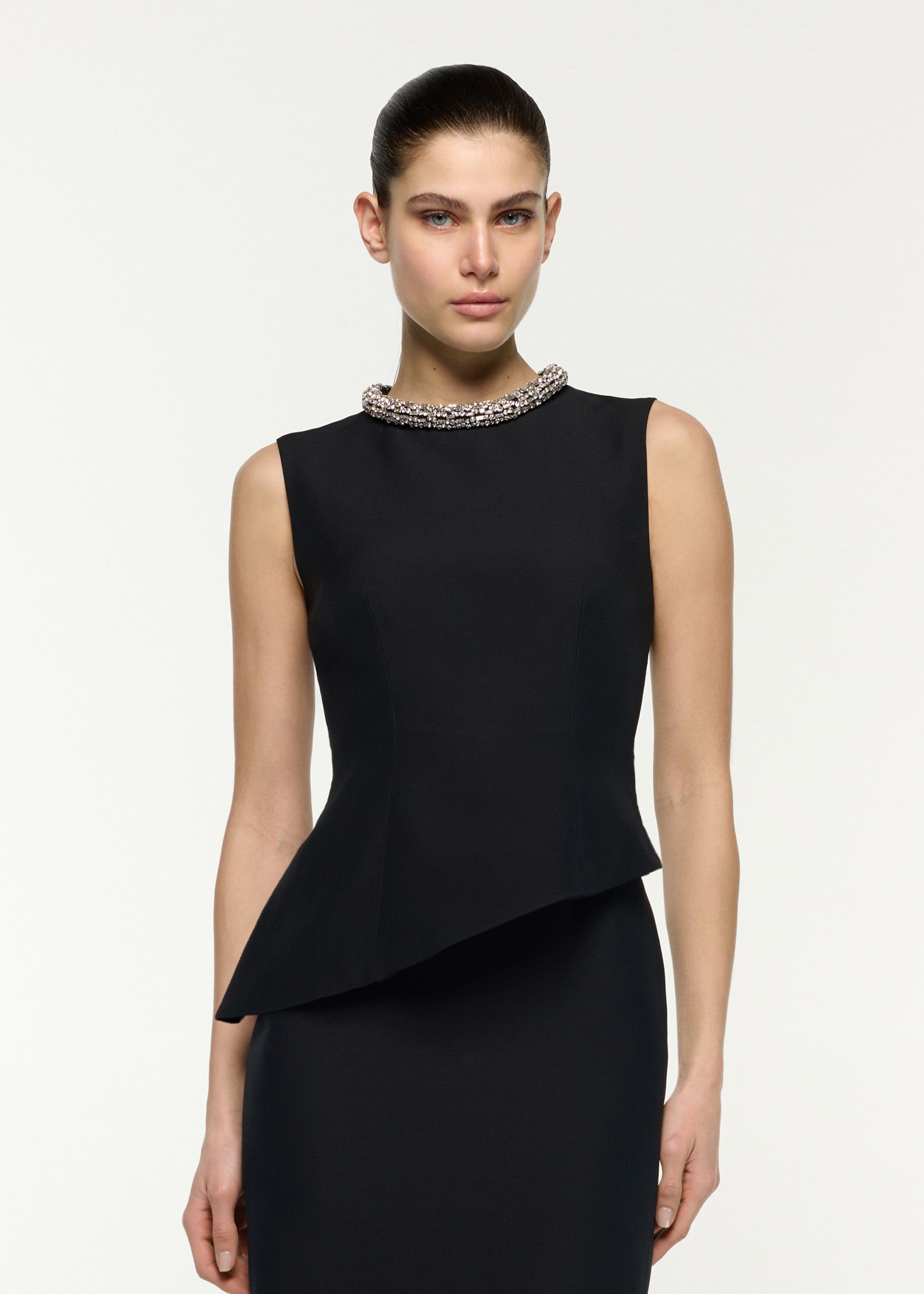 Close up of a model wearing the Crystal Neck Trimmed Asymmetric Peplum Midi Dress in Black 