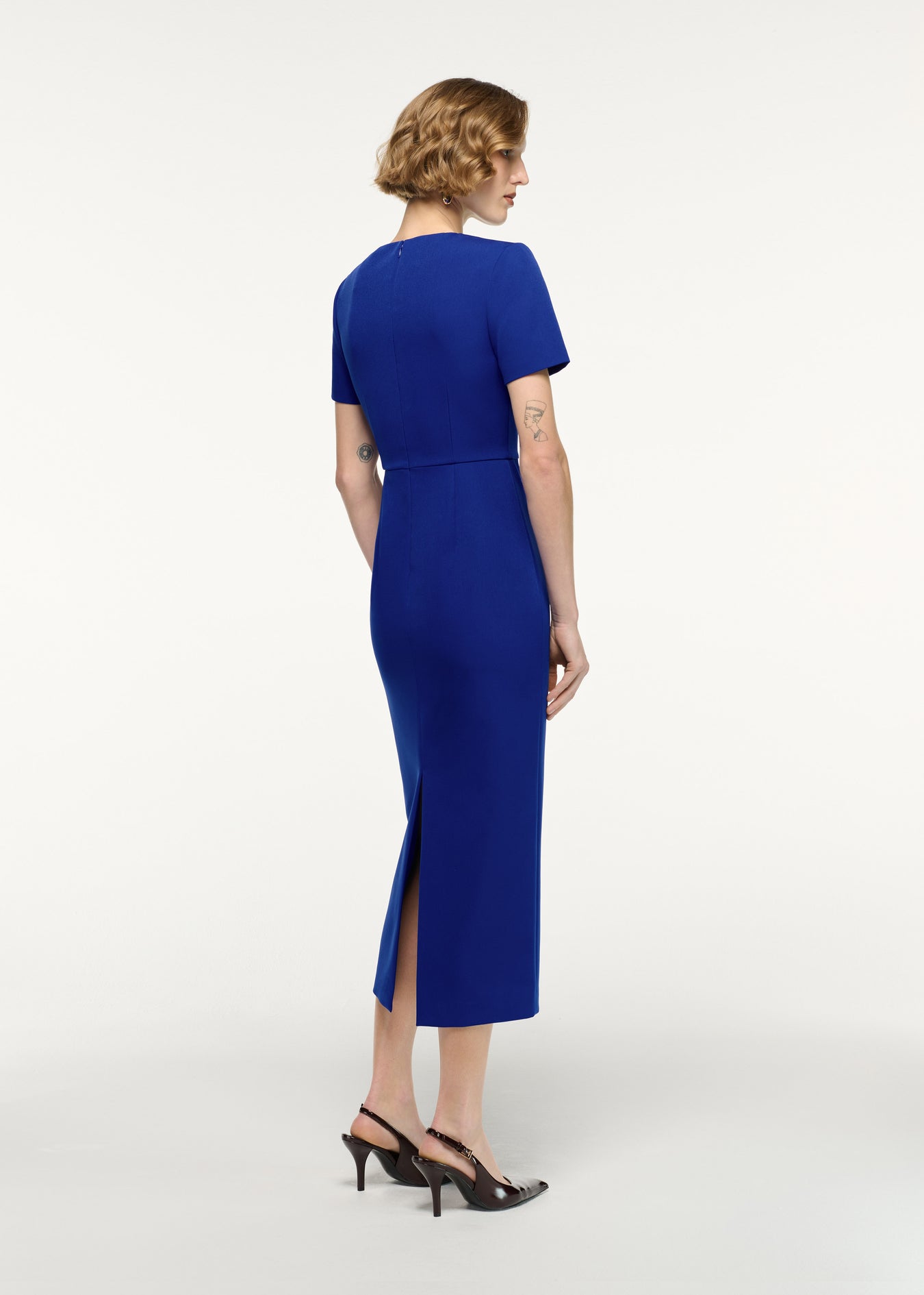 Back view of a model wearing the Asymmetric Twist Drape Midi Dress in Blue