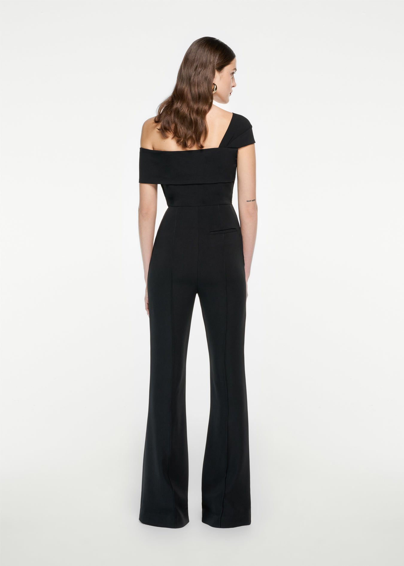 The back of a woman wearing the Asymmetric Stretch Cady Jumpsuit in Black