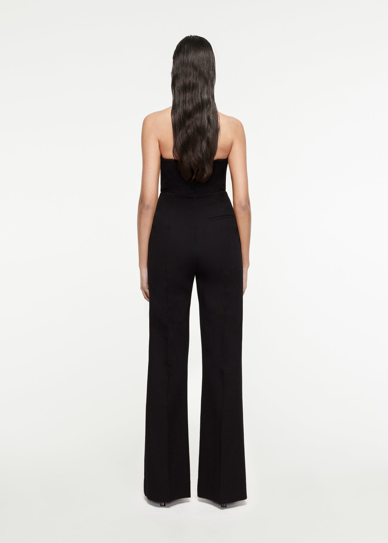 The back of a woman wearing the Asymmetric Wool Crepe Jumpsuit in Black