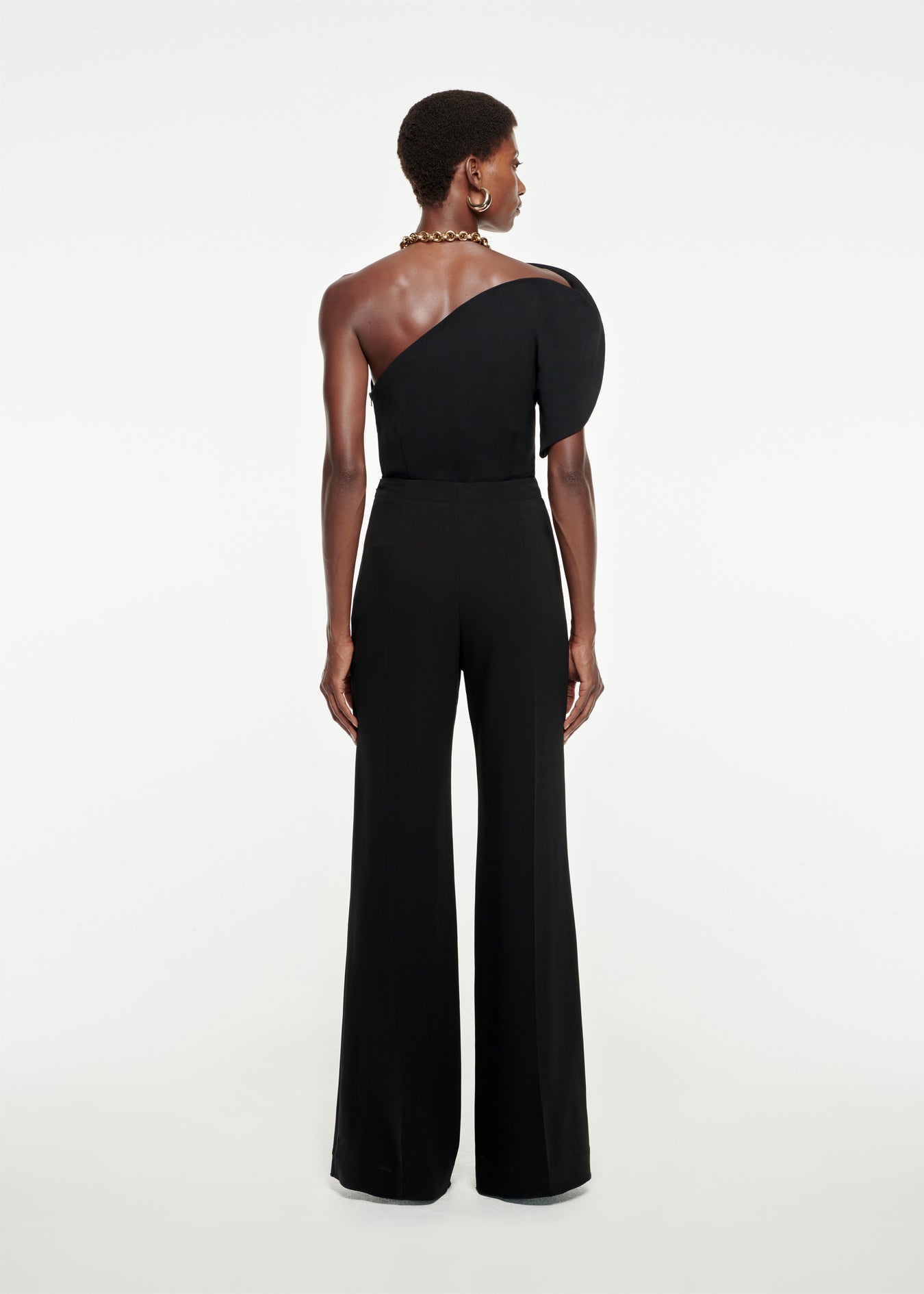The back of a woman wearing the Asymmetric Stretch-Cady Jumpsuit in Black